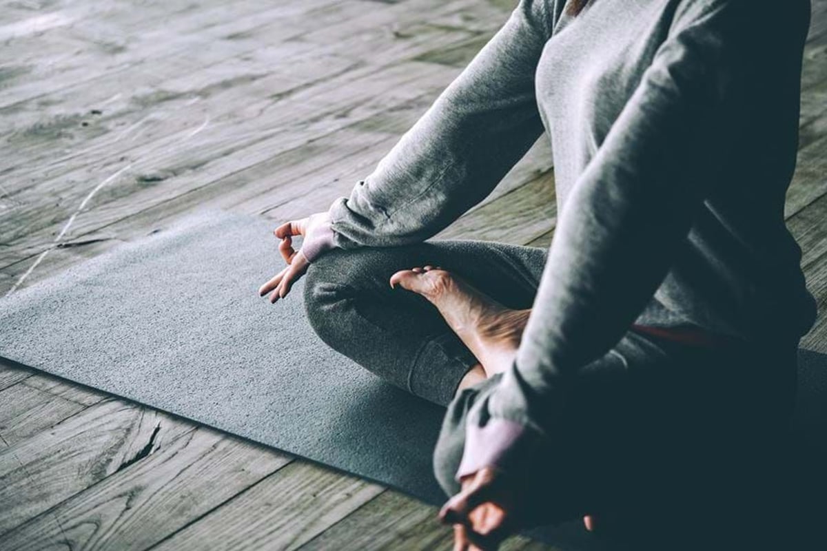 Person sitting cross-legged on a mat with hands in meditation mudra on wooden floor