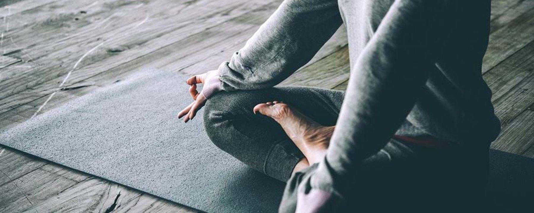 Person sitting cross-legged on a mat with hands in meditation mudra on wooden floor