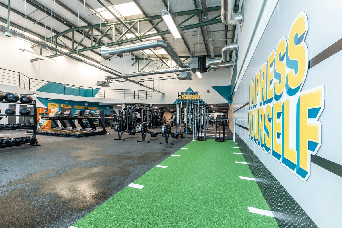 PureGym Coleraine: Weight racks, resistance machines, green turf area, exposed ceiling beams and ducts.