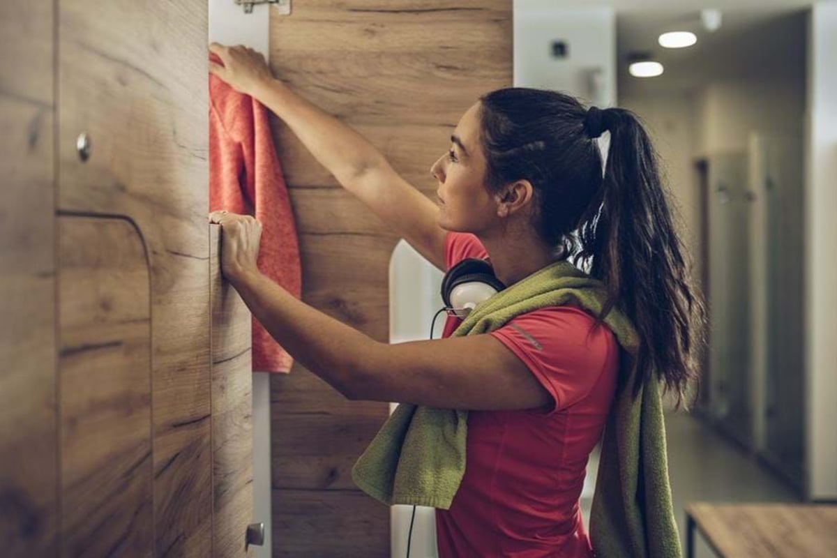 Woman hanging a red towel in a wooden locker room with a green towel around her neck.