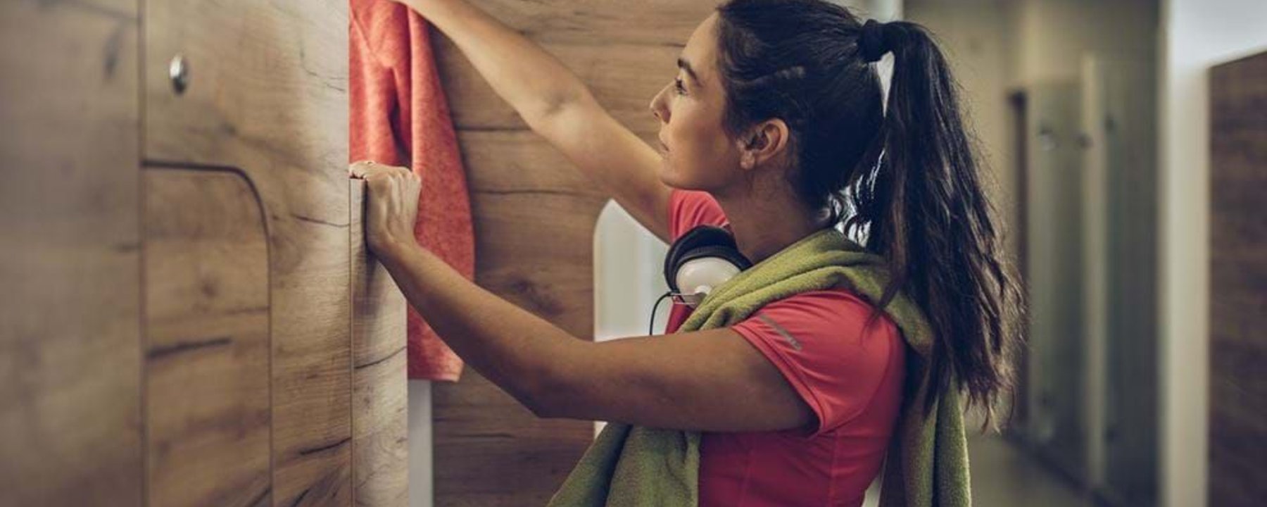 Woman hanging a red towel in a wooden locker room with a green towel around her neck.