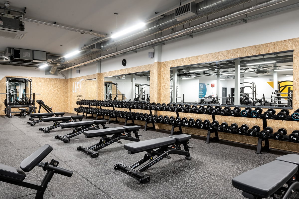 PureGym Yeovil Houndstone Retail Park: Rows of benches, free weights, rubberized flooring in a gym studio with ceiling ducts.