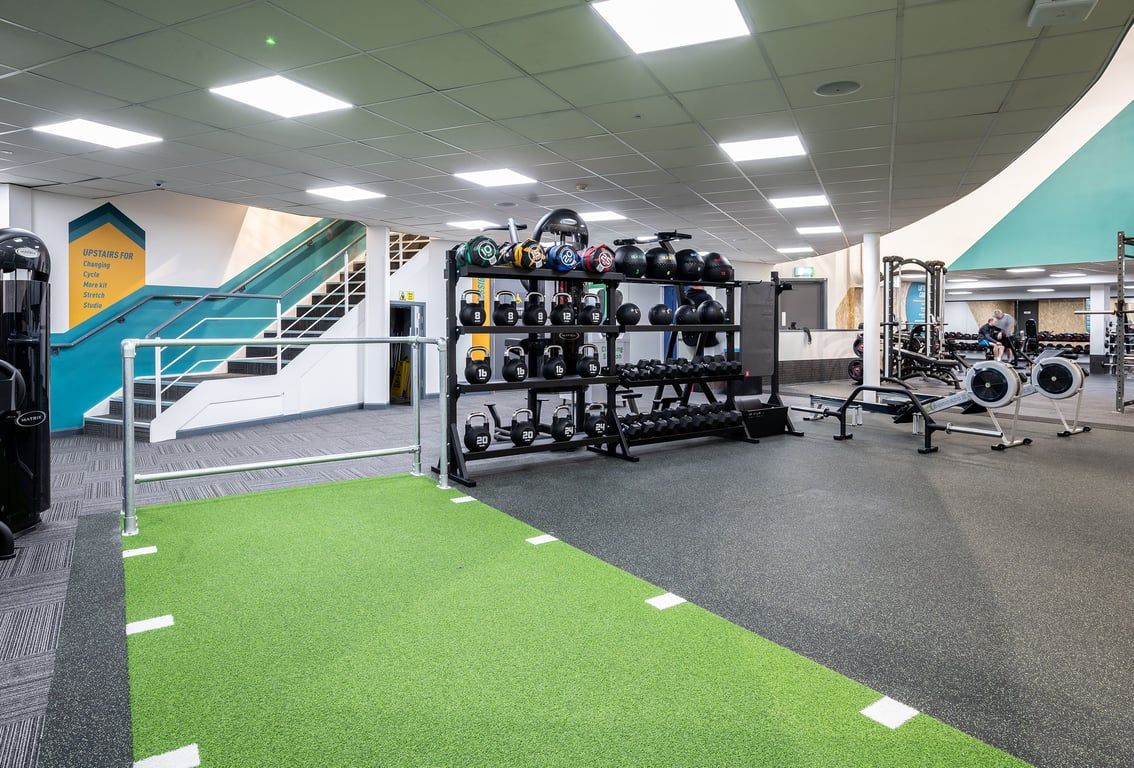 PureGym Newtownabbey: Weight racks, exercise equipment, green turf area, rubberized flooring, staircase.
