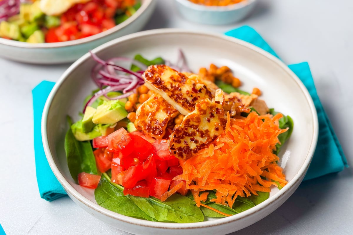 Bowl of salad with spinach, diced tomato, grated carrot, avocado, chickpeas, red onion