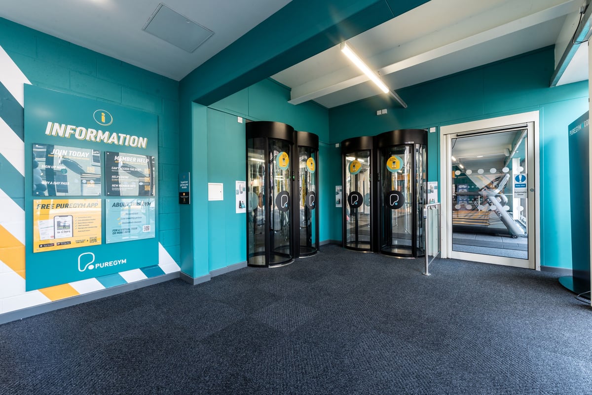 PureGym Harrogate: Entry area with turnstiles, information board, and glass doors.