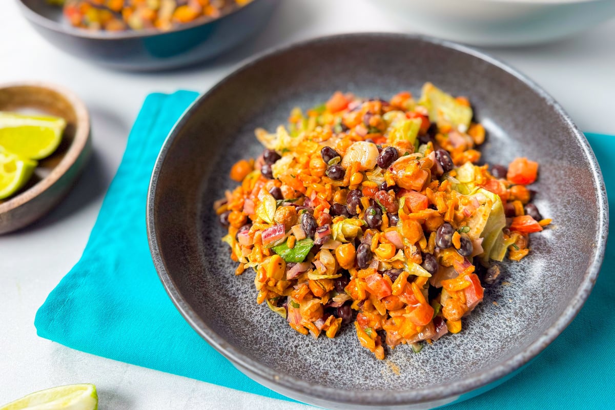 Colourful rice bowl with black beans, sweetcorn, peppers and lime wedges on the side
