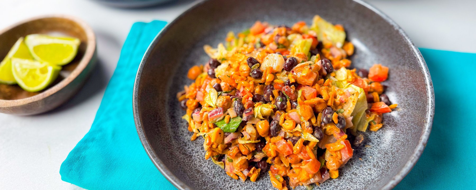 Colourful rice bowl with black beans, sweetcorn, peppers and lime wedges on the side