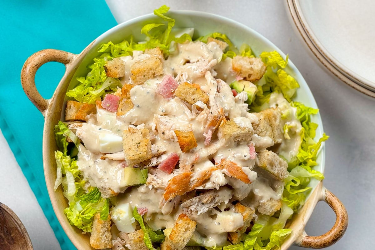 Chicken Caesar salad with croutons and dressing in a bowl on a turquoise surface