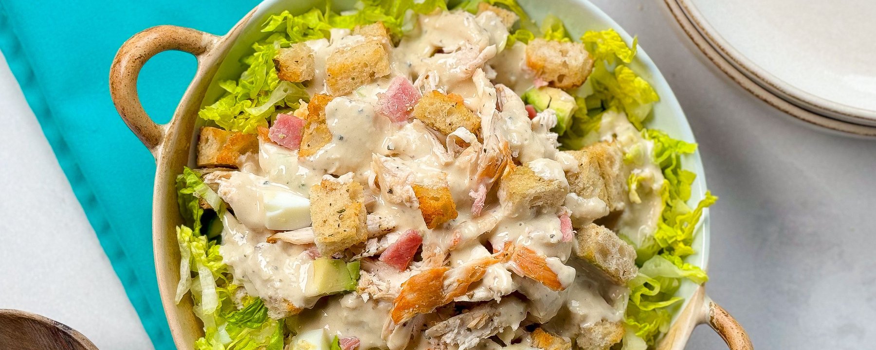 Chicken Caesar salad with croutons and dressing in a bowl on a turquoise surface