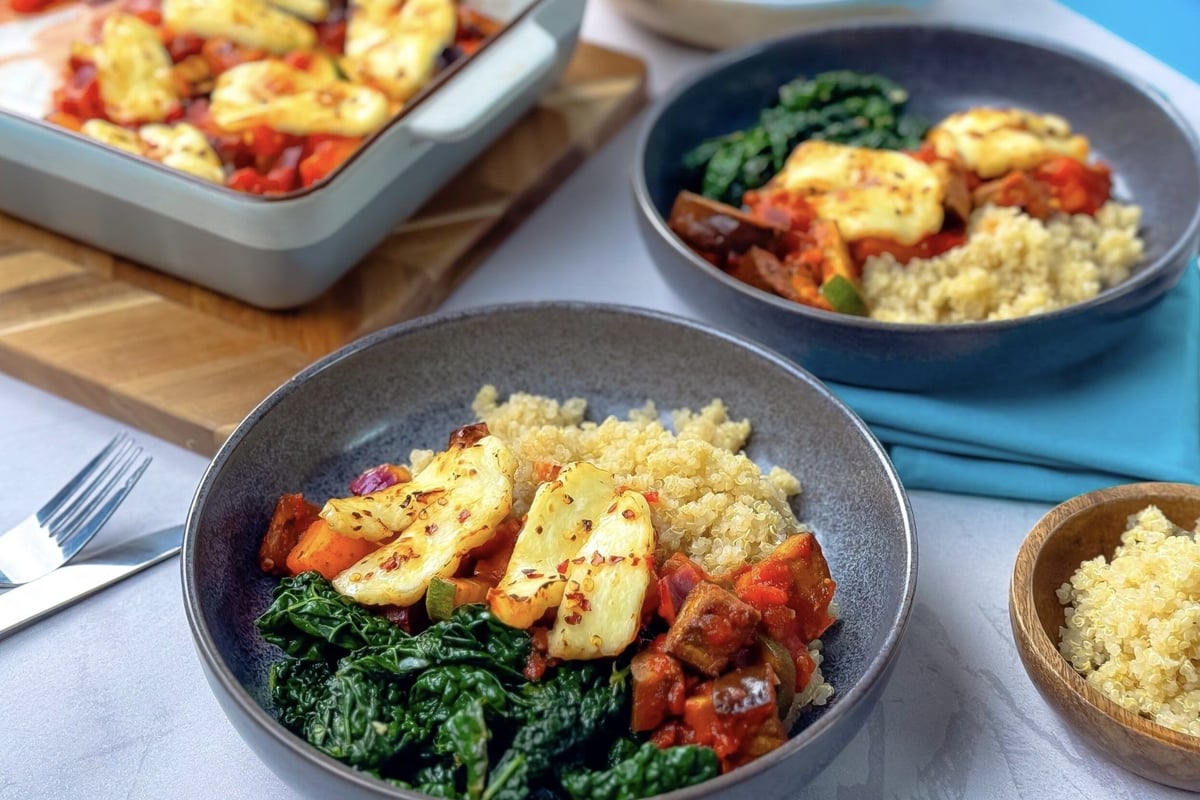 Two bowls with quinoa, cooked kale, roasted vegetables, and grilled halloumi cheese.