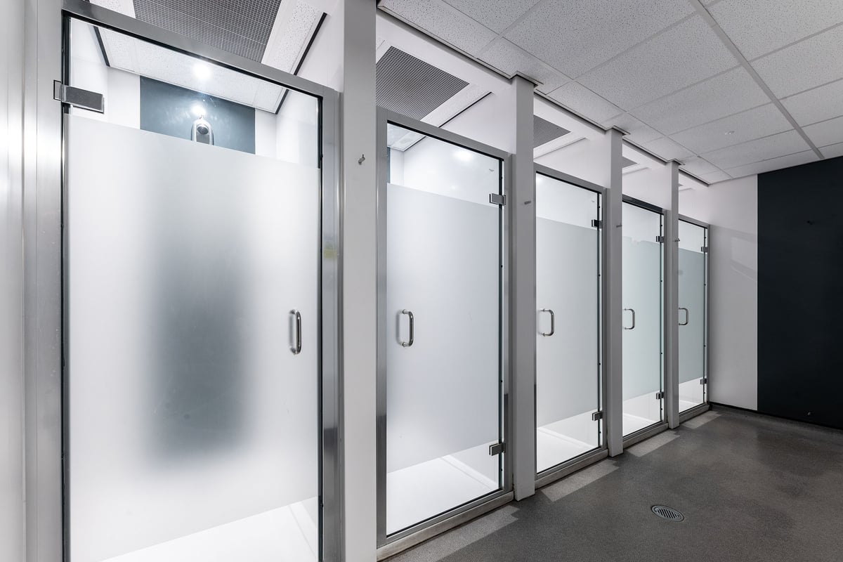 PureGym Leamington Spa: Rows of glass-enclosed, frosted shower or changing cubicles with metallic frames.