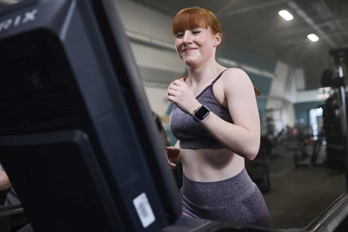 Jeune femme en tenue de sport courant sur un tapis roulant en salle de sport