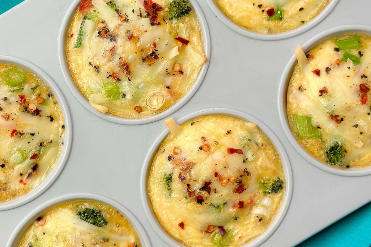 Six egg muffins with vegetables and cheese in a grey muffin tray on a turquoise cloth