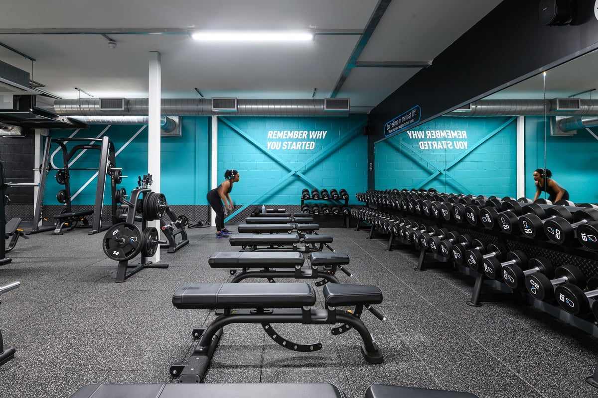 PureGym St Albans: Rows of weight benches, dumbbells, weight racks, and rubberized flooring in a teal-accented gym studio.
