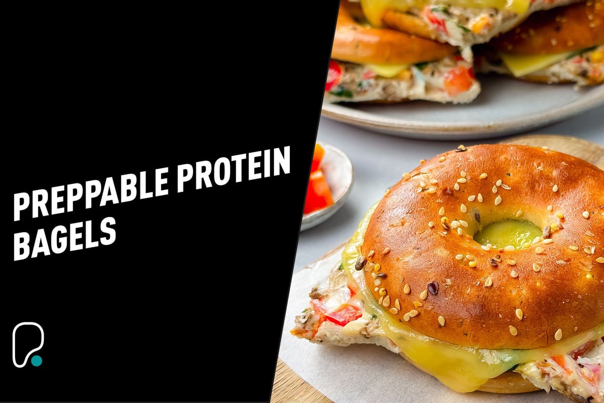 Sesame seed bagel sandwich with melted cheese and vegetable cream filling on a wooden board