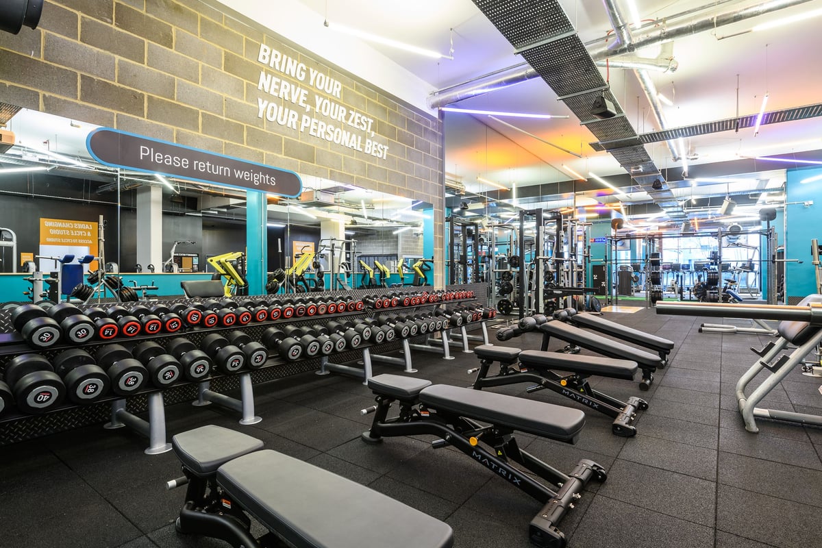 PureGym London Borough: Rows of weight benches, free weights, weight racks, and motivational signage on brick wall.