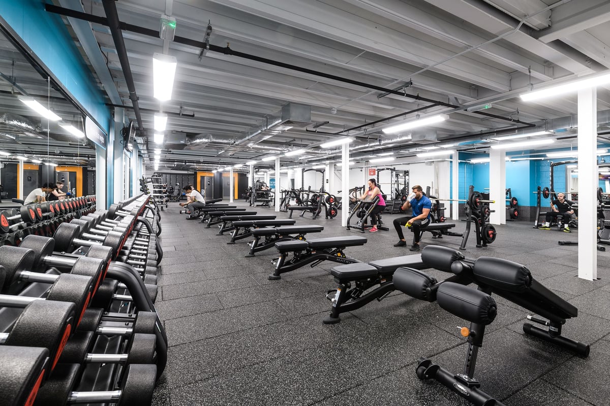 PureGym Glasgow Silverburn: Rows of weight benches, racks, dumbbells, and rubberized flooring in a brightly lit gym.