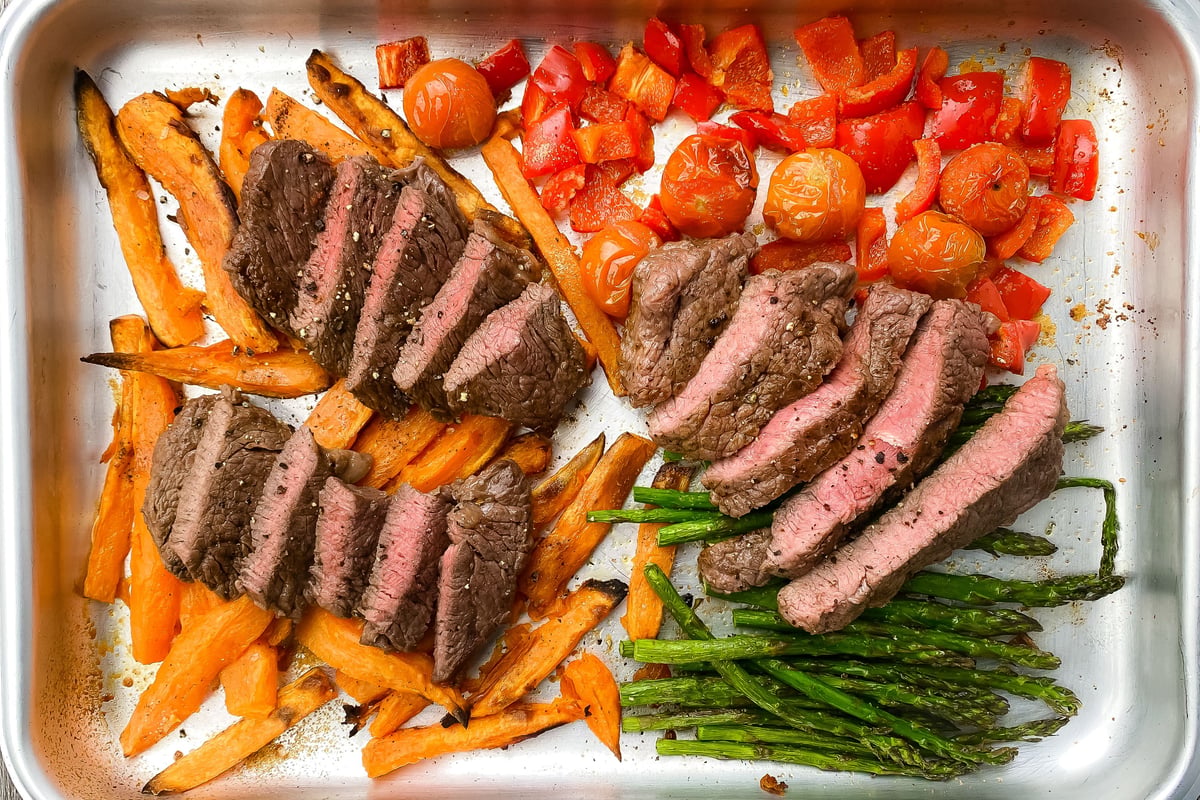Sliced steak with roasted peppers, tomatoes, sweet potato and asparagus on a baking tray