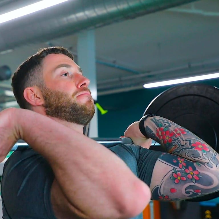 Man with tattoo lifting barbell in gym with focused expression