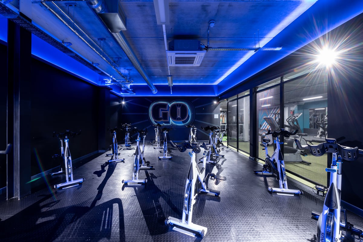 PureGym Plymouth Marsh Mills: Rows of stationary bikes and elliptical machines in a dimly lit studio with blue neon lighting.