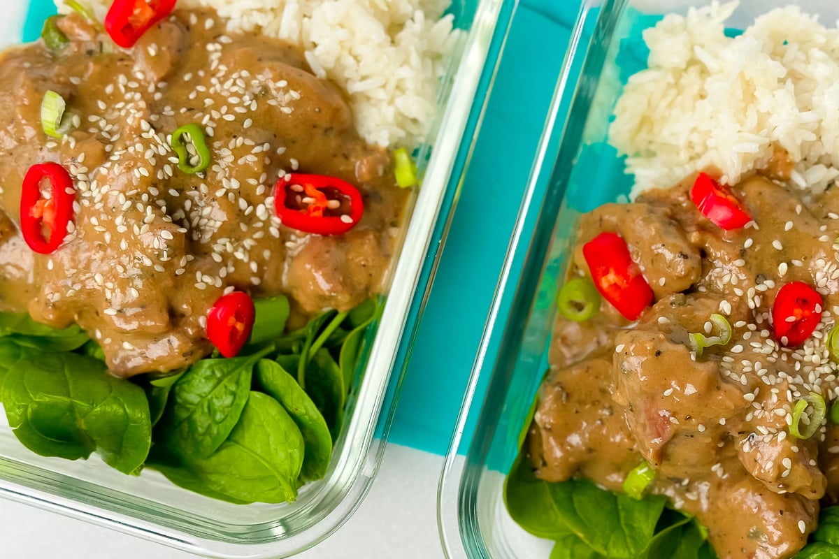 Two meal prep containers with glazed lamb, white rice, spinach, sesame seeds and chillies