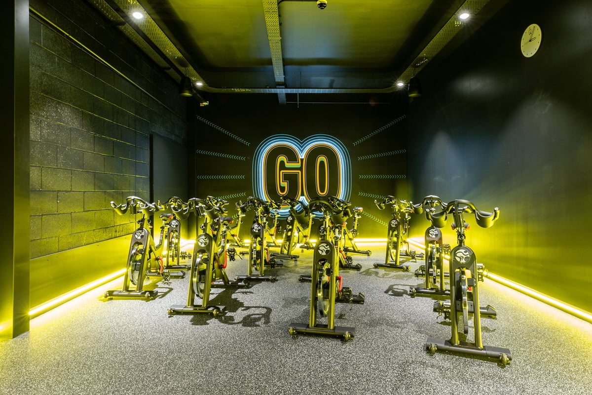 PureGym Redditch Ringway: Rows of stationary exercise bikes illuminated by neon "GO" signage.