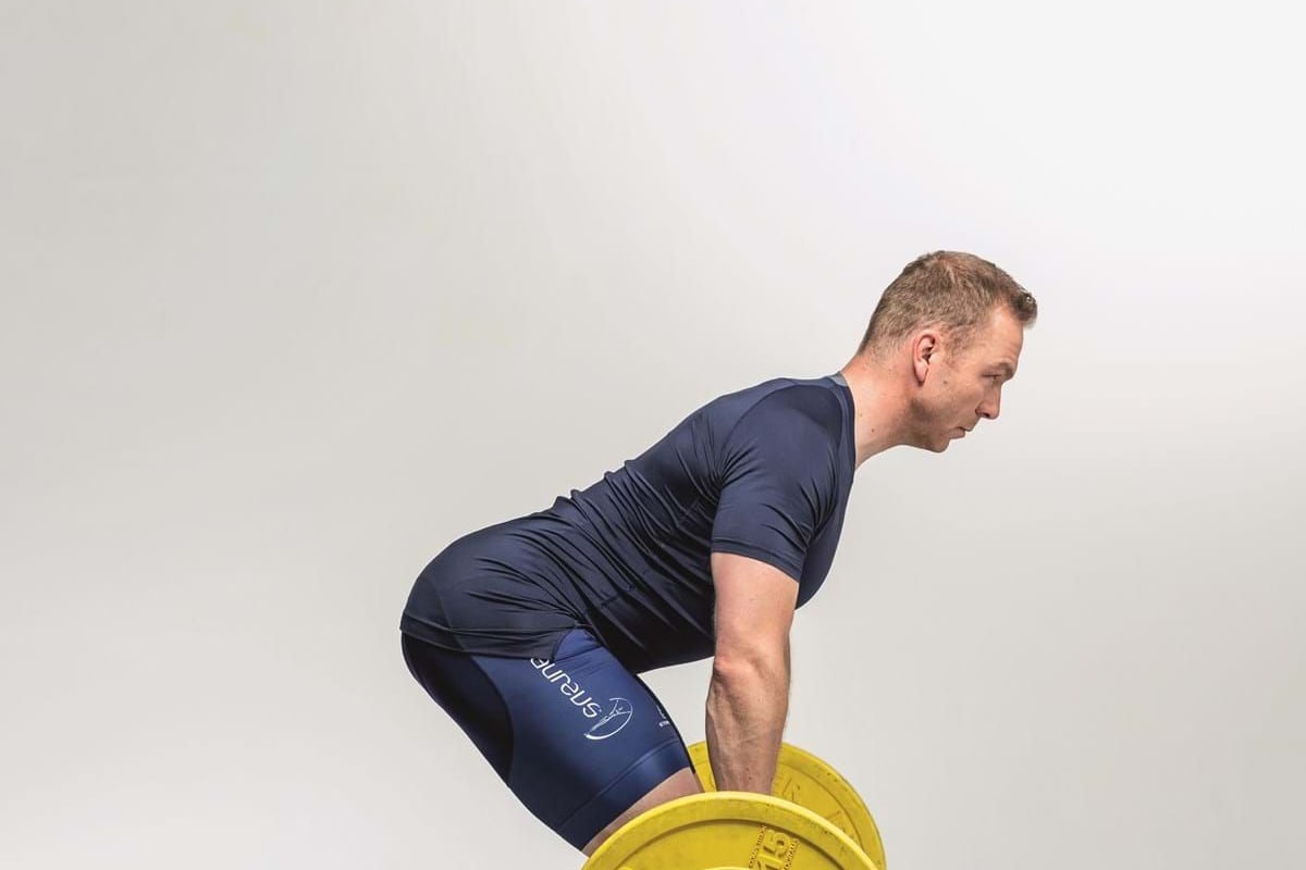 Man in sportswear lifting a barbell with yellow weights in a studio setting