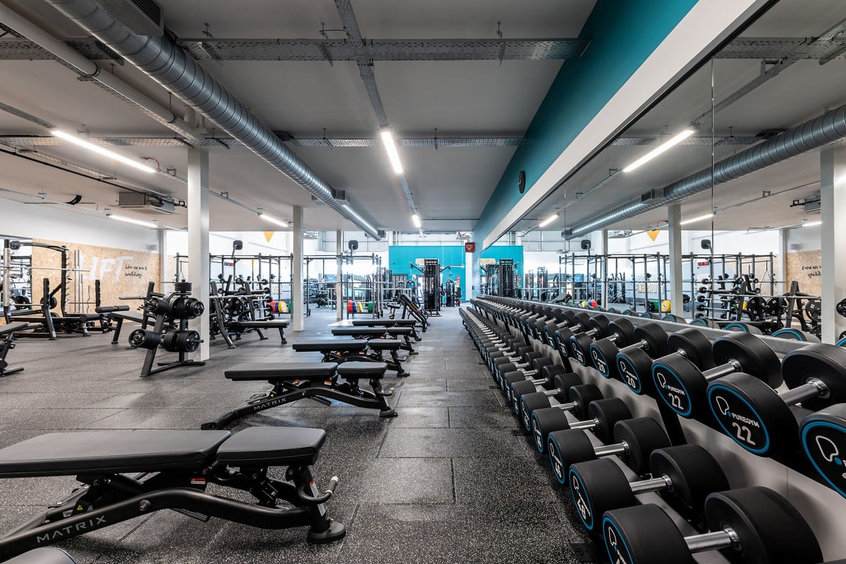 PureGym Consett: Weight benches, dumbbell racks, resistance machines, and dark teal accent paint in a spacious gym interior.