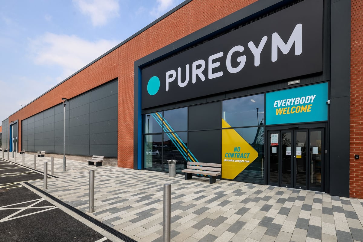 PureGym Bishop Auckland: Gym building exterior with large signage, outdoor seating, and parking area.