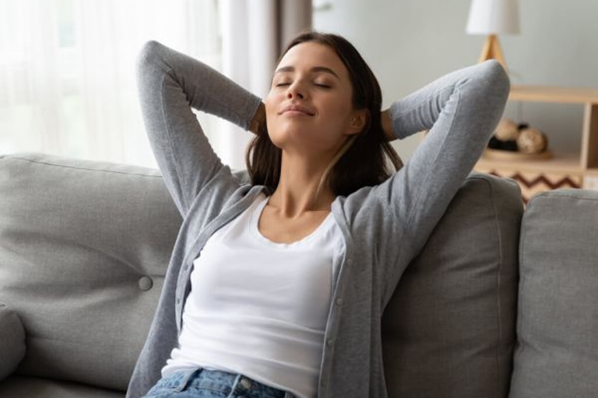 Femme en haut blanc et gilet gris, détendue sur un canapé, yeux fermés