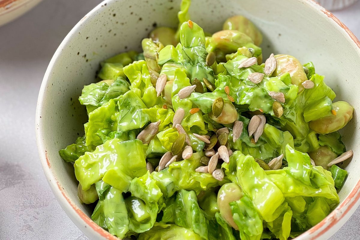 Green salad with broad beans and pumpkin seeds in a speckled ceramic bowl