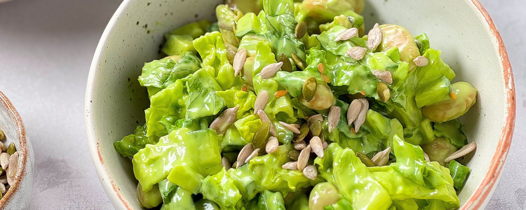 Green salad with broad beans and pumpkin seeds in a speckled ceramic bowl
