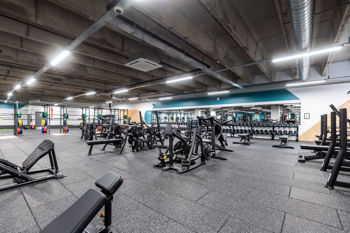 PureGym London Ealing Broadway: Rows of weight machines, benches, free weights, and rubberized flooring in a dimly lit gym.