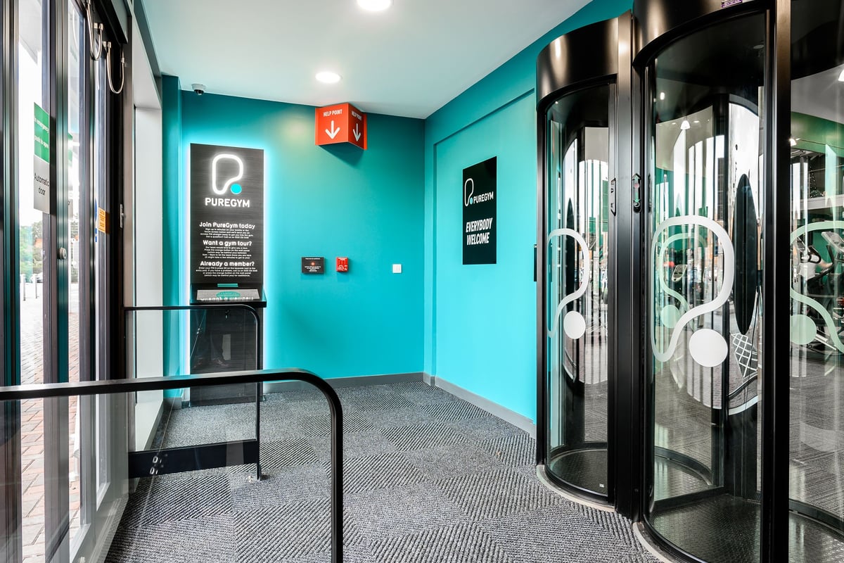PureGym Exeter Bishops Court: Rows of upright pods with glass doors, turquoise walls, laminate flooring.