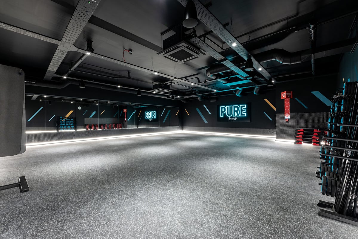 PureGym Blyth: Weight racks, benches, mirrors, rubberised flooring in dimly lit strength training area.