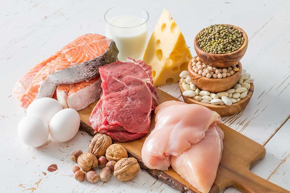 Proteinreiche Lebensmittel auf weißem Holz: Lachs, Rind, Huhn, Eier, Käse, Milch, Nüsse