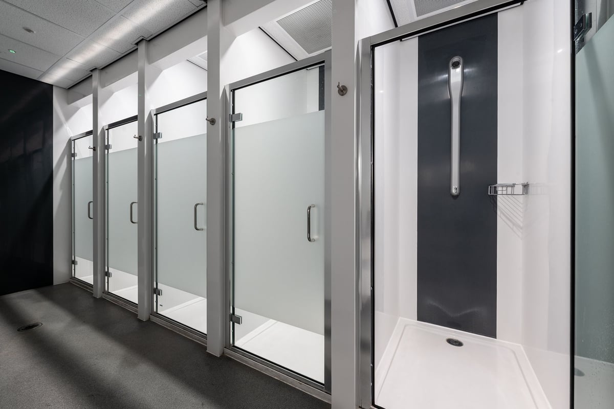 PureGym Stevenage: Glass-walled shower stalls, tiled floors in a gym changing room.