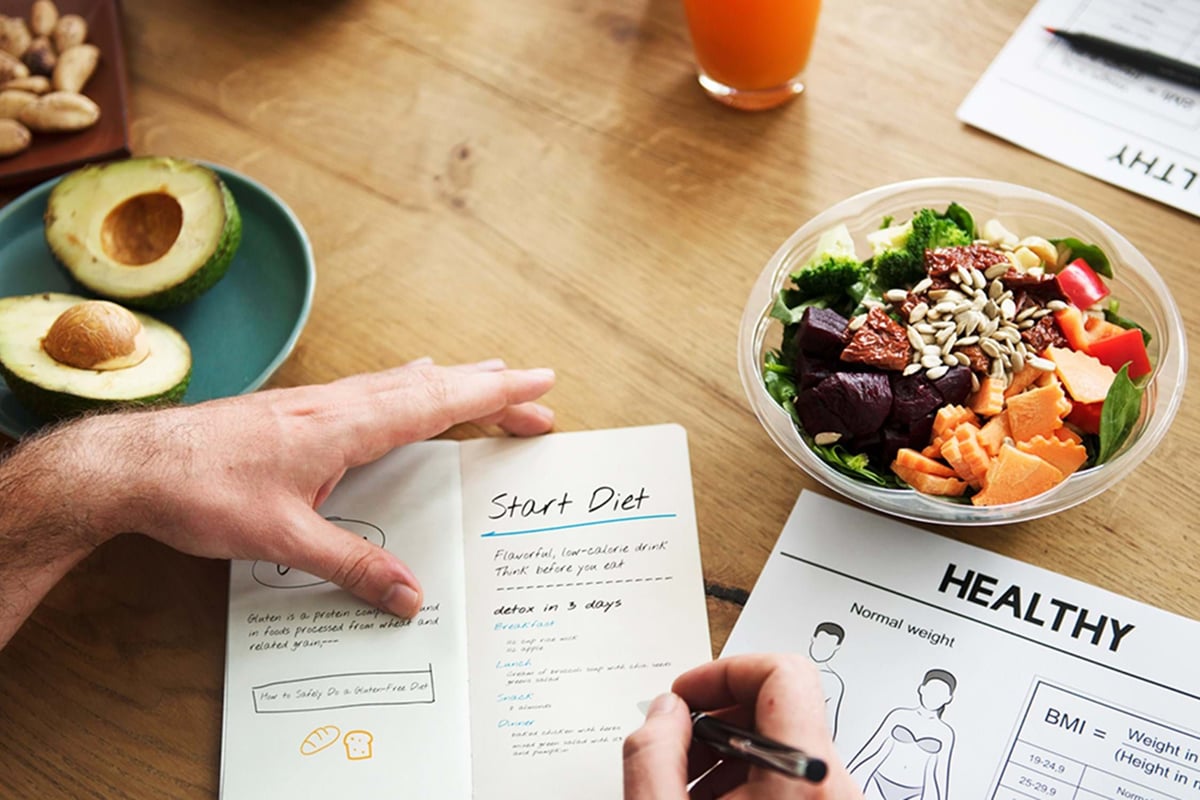 Hand writing diet plan with avocado, nuts, salad bowl, and juice on wooden table