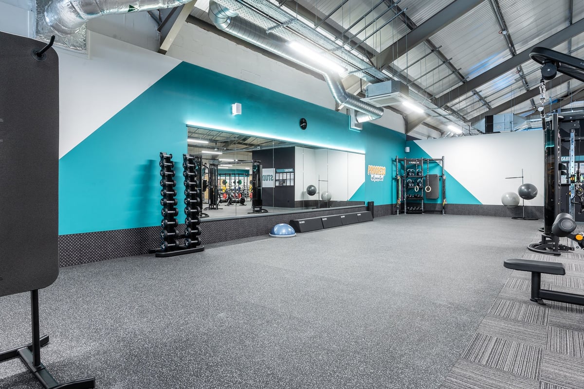 PureGym Derby Meteor Centre: Weights benches, resistance machines, turf area, mirrored wall in teal and grey tones.