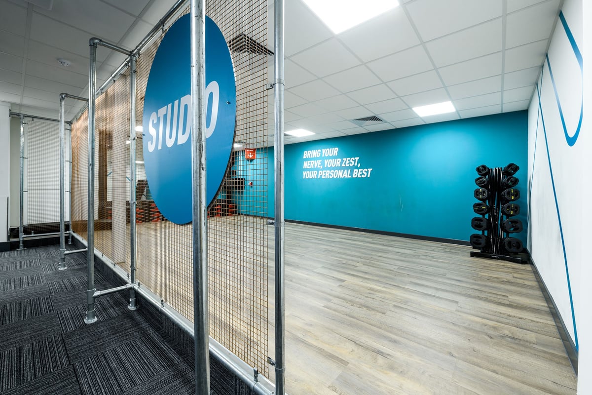PureGym London Bow Wharf: Glass-walled exercise area with blue branding, wire mesh partitions, and patterned flooring.