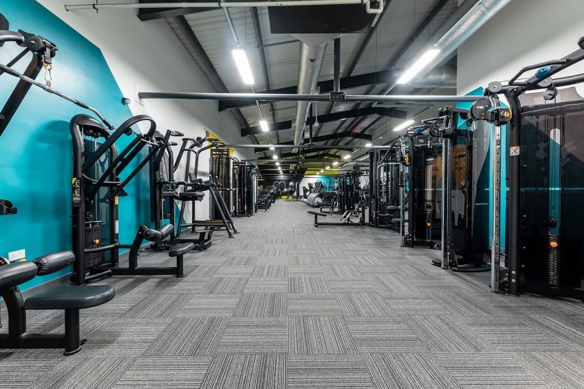 PureGym Ashton Under Lyne: Rows of resistance machines, benches, turquoise equipment, and industrial ceiling fixtures.