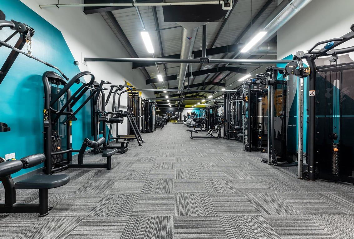 PureGym Ashton Under Lyne: Rows of resistance machines, benches, turquoise equipment, and industrial ceiling fixtures.