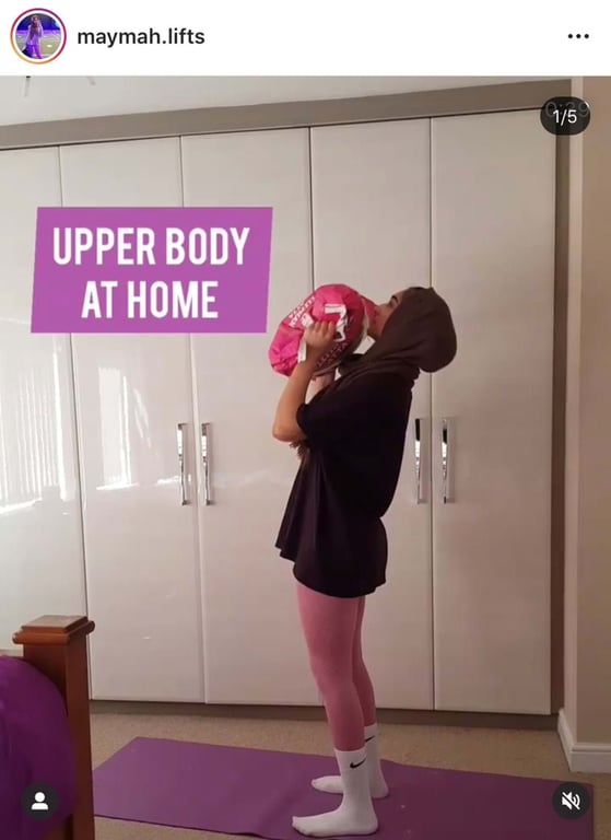 Woman in hijab lifting a pink bag on a purple mat in a bedroom with white wardrobes