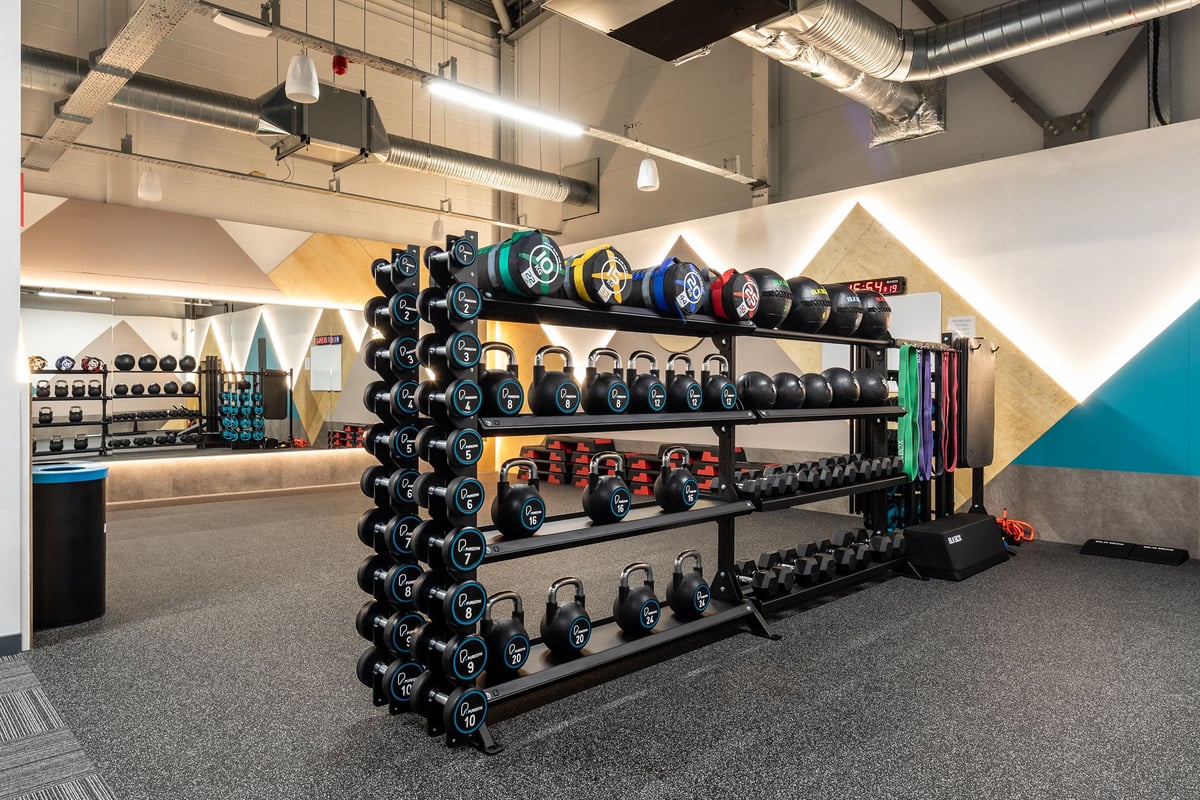 PureGym Wantage: Racks of dumbbells, weight plates in various colours, and mirrored walls in a gym setting.