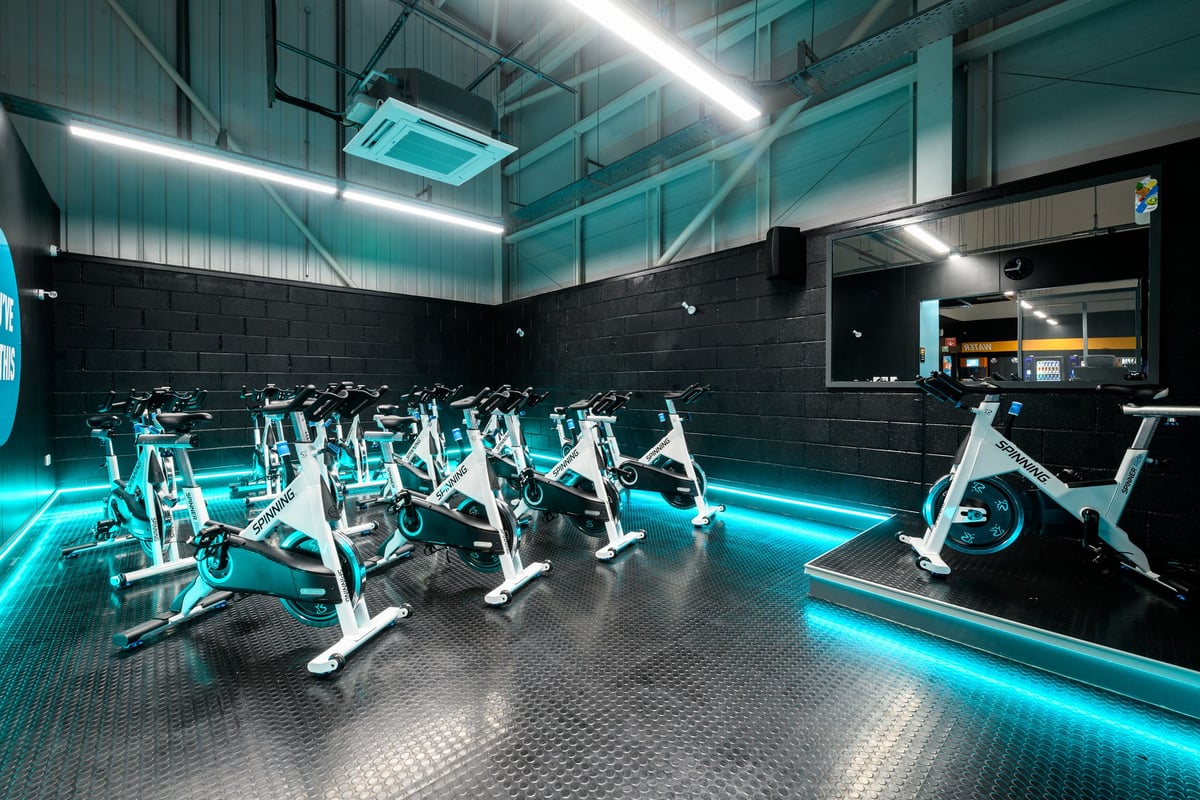 PureGym Nottingham Castle Marina: Rows of stationary bikes illuminated by teal neon lighting in a sleek gym studio.