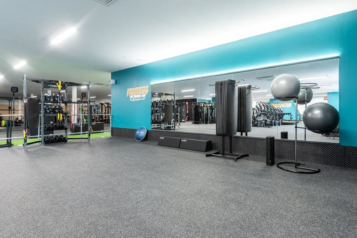 PureGym Knaesborough: Fitness studio with weight racks, medicine balls, benches, rubberized floors, and teal accent walls.