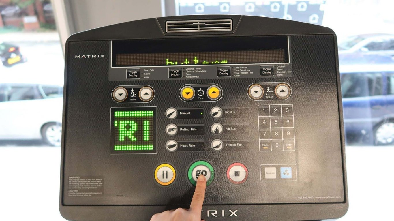 Hand pressing green go button on treadmill control panel with digital display and buttons