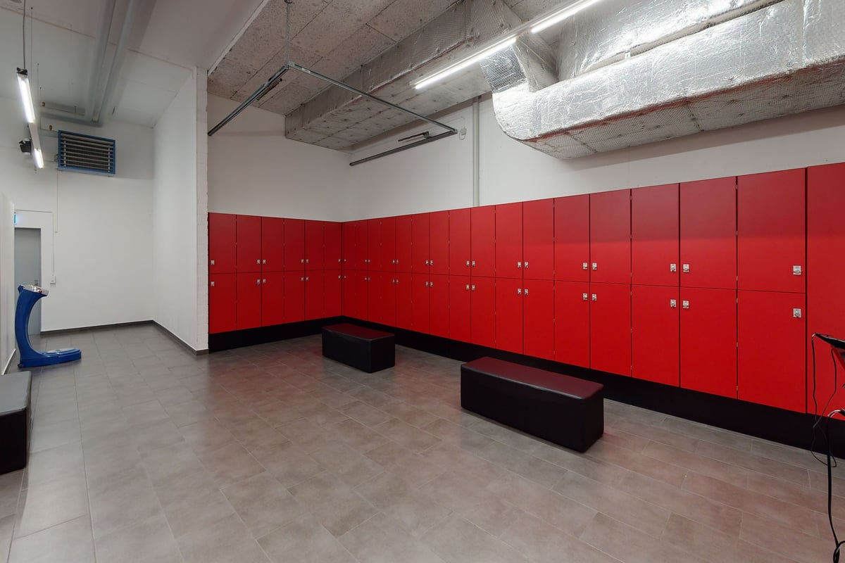 PureGym Pfäffikon: Rote Schränke, Bänke und Betonböden in einem Umkleideraum oder Umkleideraum im Innenbereich.