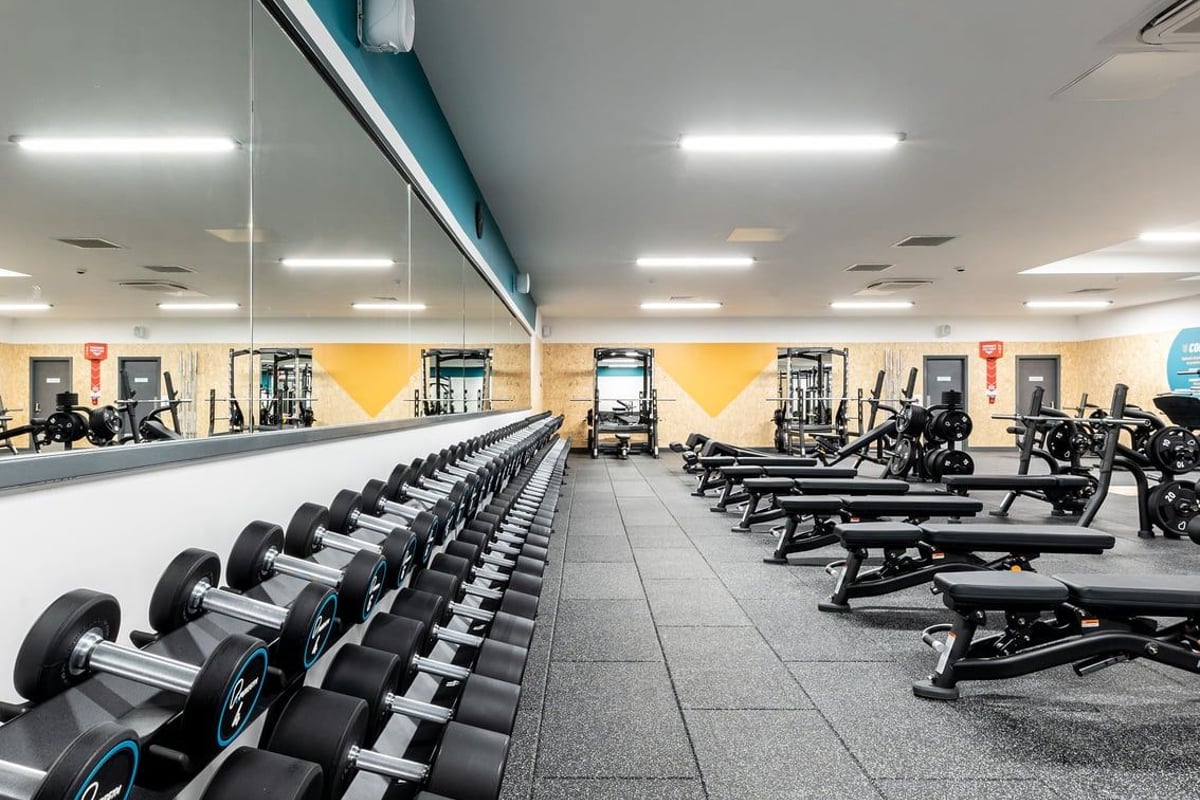 PureGym Bangor Wales: Rows of dumbbell racks, weight benches, and exercise machines in a brightly lit fitness centre.