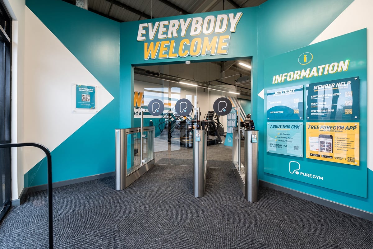 PureGym Newhaven: The gym entrance with turnstiles, directional signage, and tiled flooring.